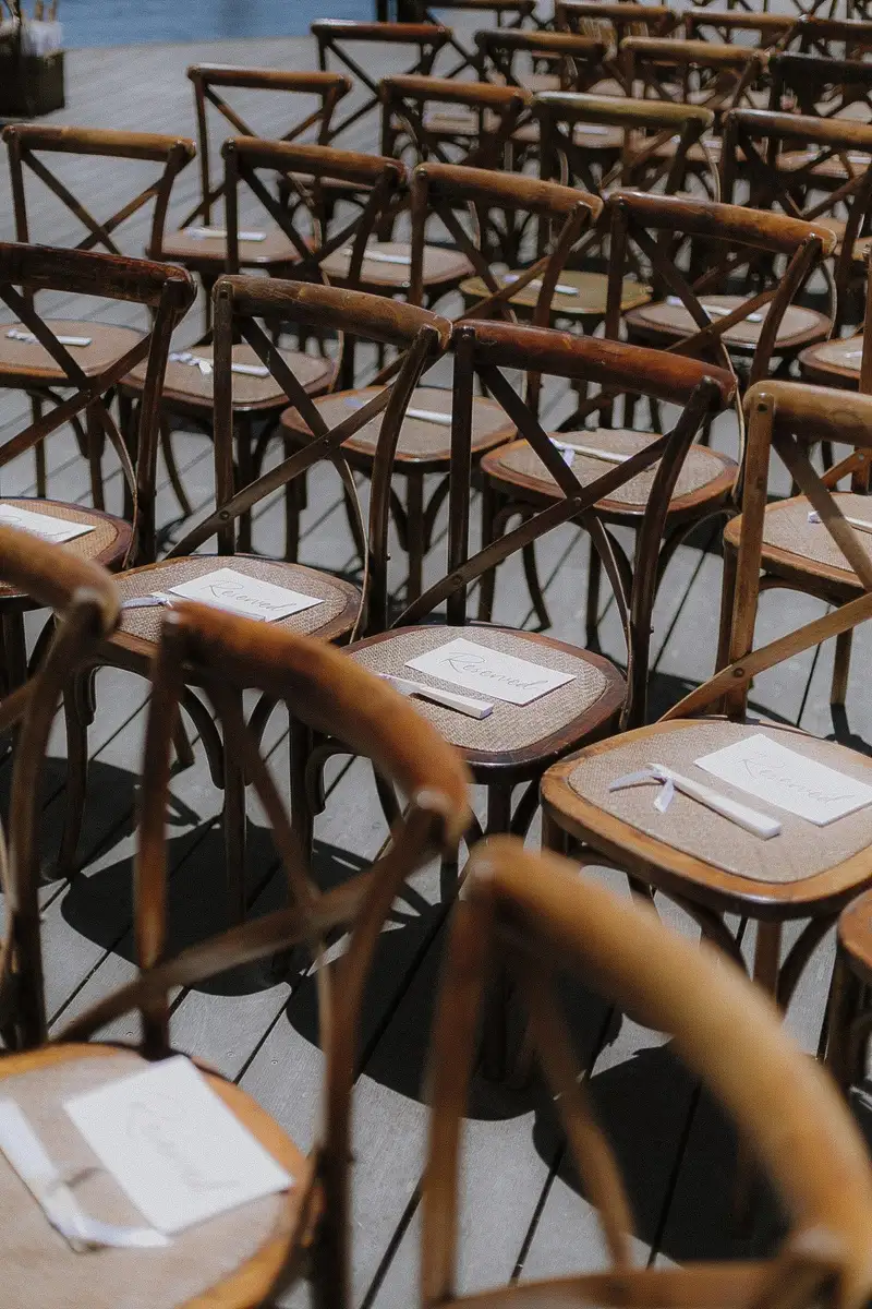 Wooden cross-back ceremony chairs with folded order-of-service cards on each seat