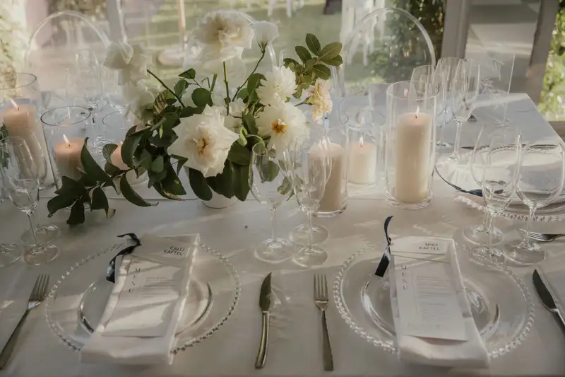 Menus and place cards on glass charger plates with white florals and candles