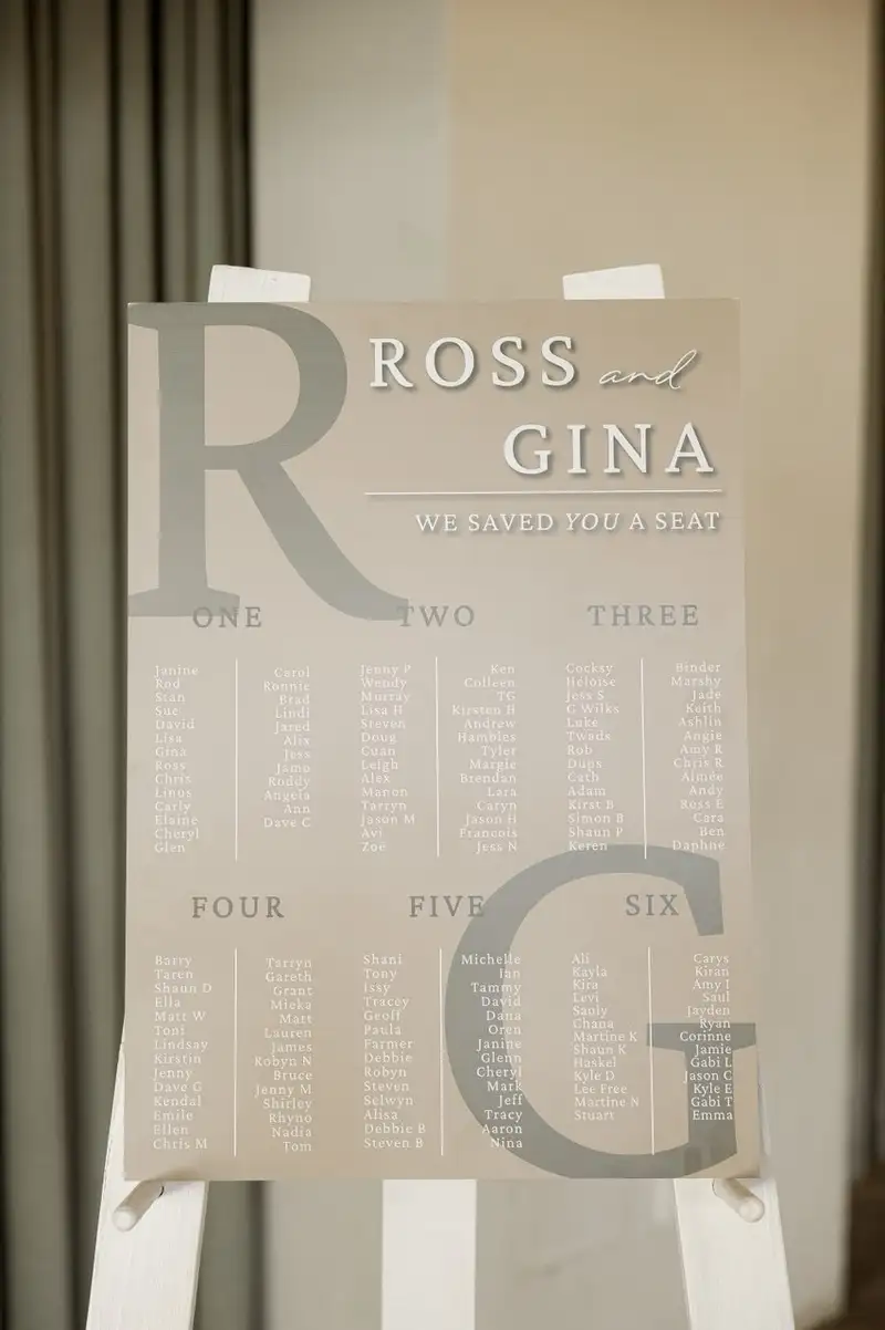 Frosted acrylic seating chart with large initials, standing on a glass surface